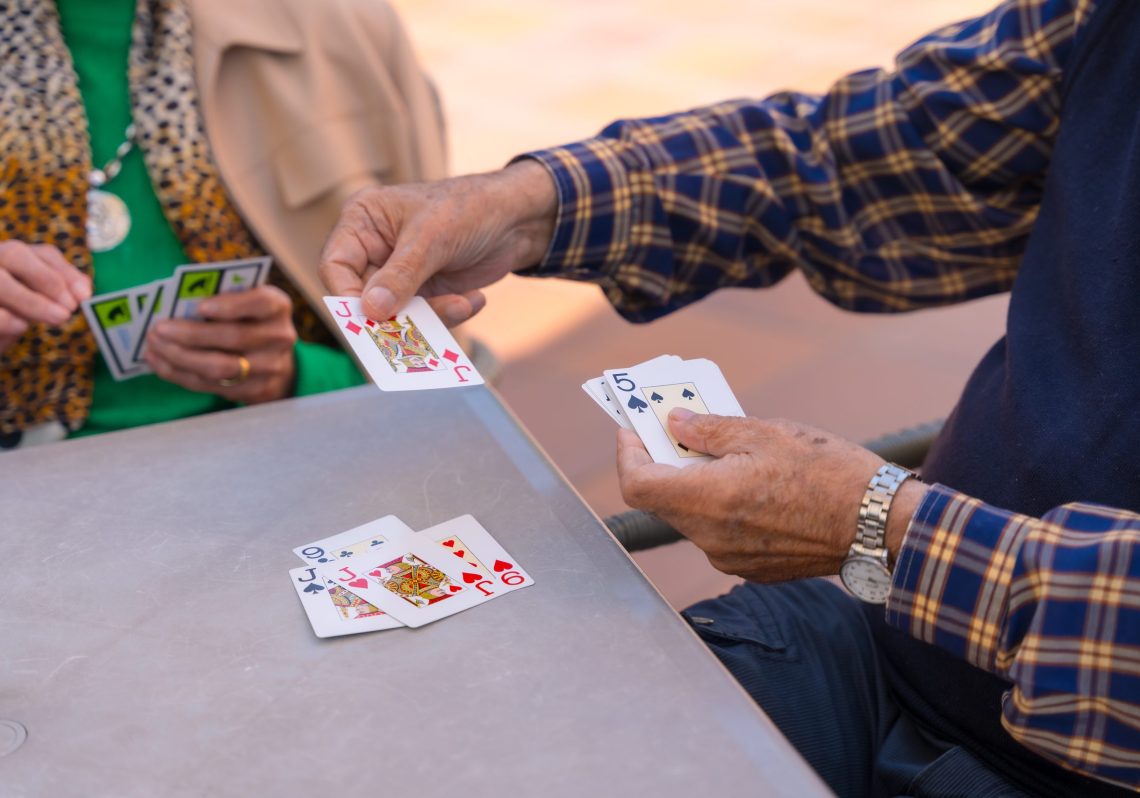 Hands of two elderly people in the garden of a nursing home or retirement home playing cards on a summer morning